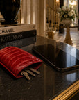 A red crocodile-embossed leather key pouch holding keys, placed on a polished black marble counter next to a black smartphone in a luxury interior setting.